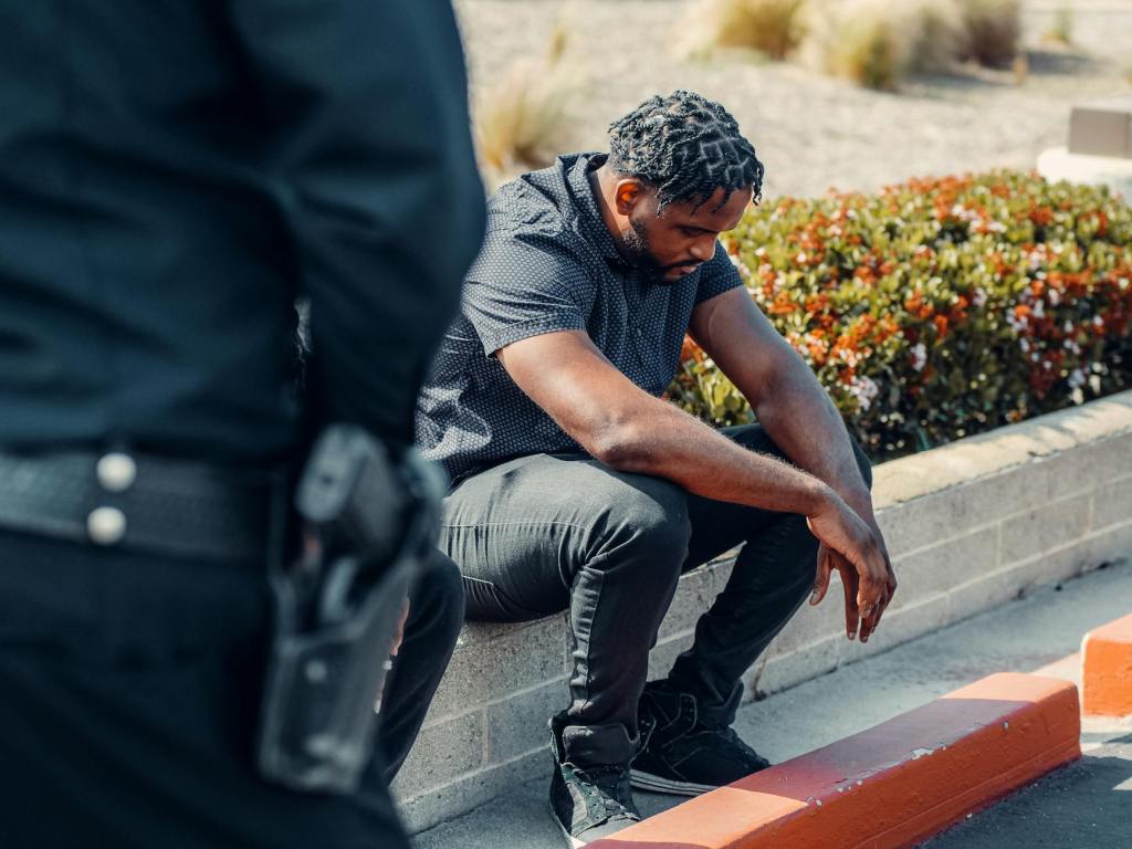 man in gray button up shirt and gray denim jeans sitting on concrete block beside a police officer